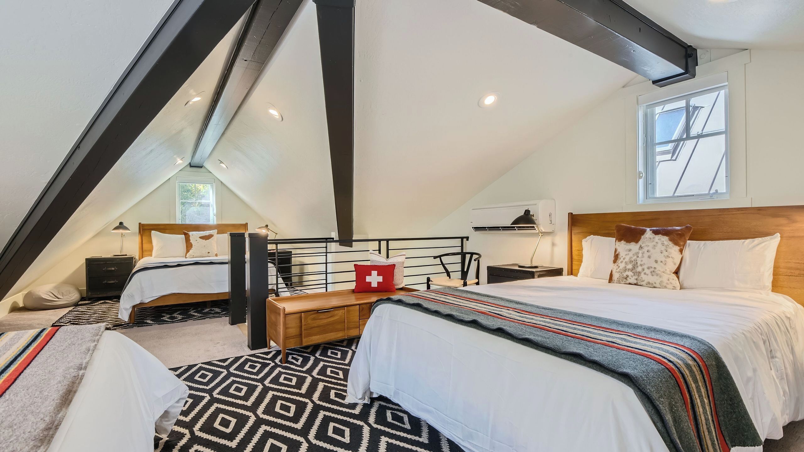 Un dormitorio con techo inclinado, dos camas, cabecero de madera, un banco y una alfombra estampada.