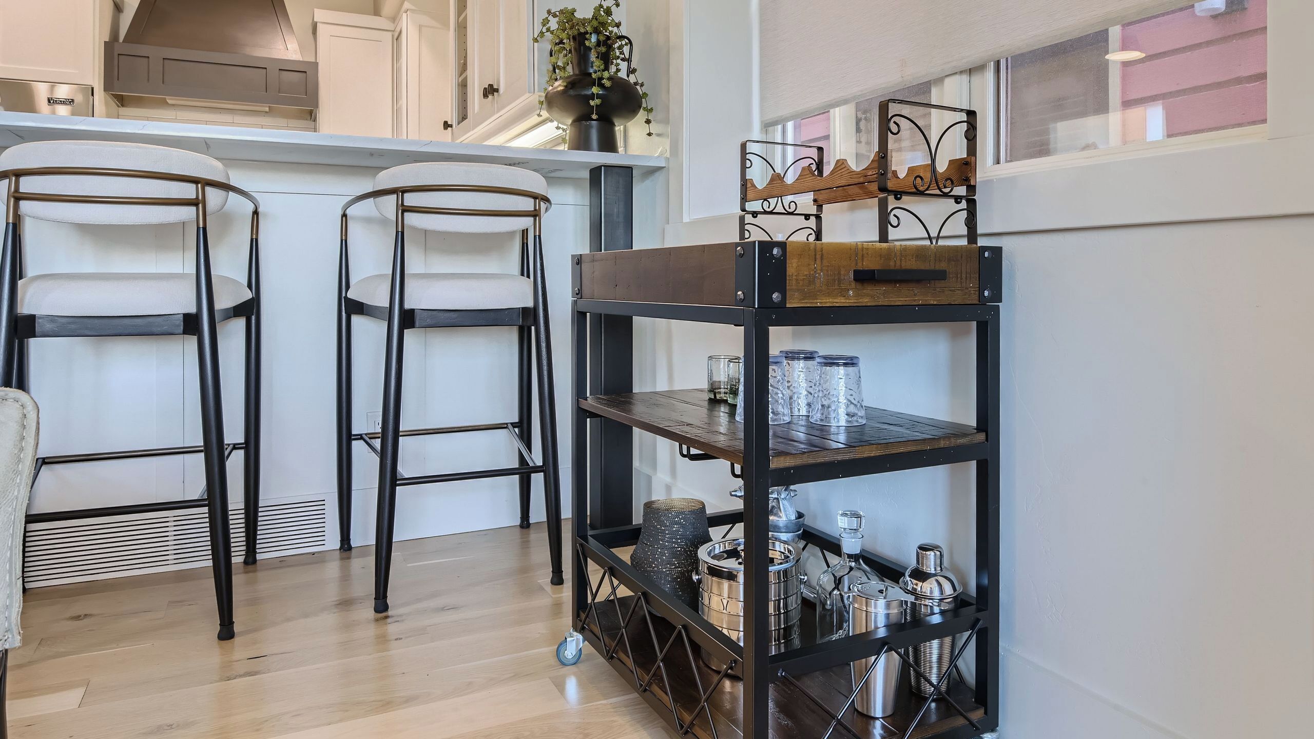 Une cuisine avec deux tabourets de bar, une étagère en métal et une plante en pot.