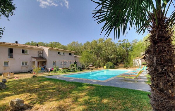 Ein Pool mit glatter, blauer Wasseroberfläche, eine Palme und ein Gebäude mit einem Ziegeldach.