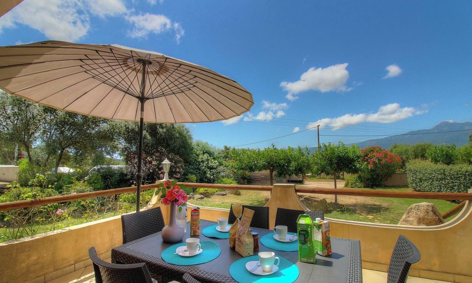 An outdoor dining area with a table, chairs, an umbrella, and a view of the landscape.