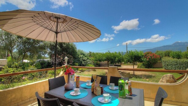 Un área de comedor al aire libre con una mesa, sillas, un paraguas y vistas del paisaje.