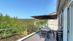 Un balcone con tavolo e sedie, un ombrellone grande e vista su un paesaggio collinare.