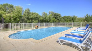 Ein rechteckiger Pool mit weißem Zaun, umgeben von Liegestühlen und Bäumen.