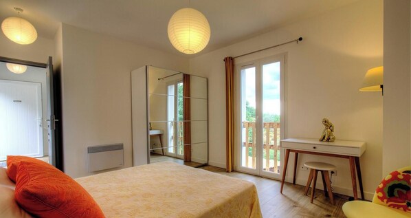 Ein Schlafzimmer mit Bett, Schreibtisch und Stuhl. Eine Schiebetür führt zu einem Balkon.