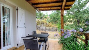 Un porche techado con una mesa y sillas, una valla de madera y vistas a un jardín con árboles y flores.