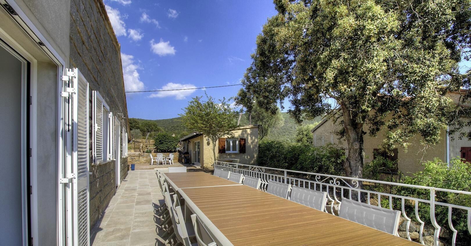 A narrow corridor with a wooden deck, white railings, and a view of a hillside.