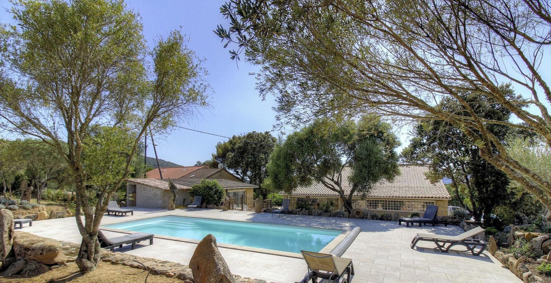 Una piscina con sillas de descanso, un patio de piedra y una casa con techo de tejas.