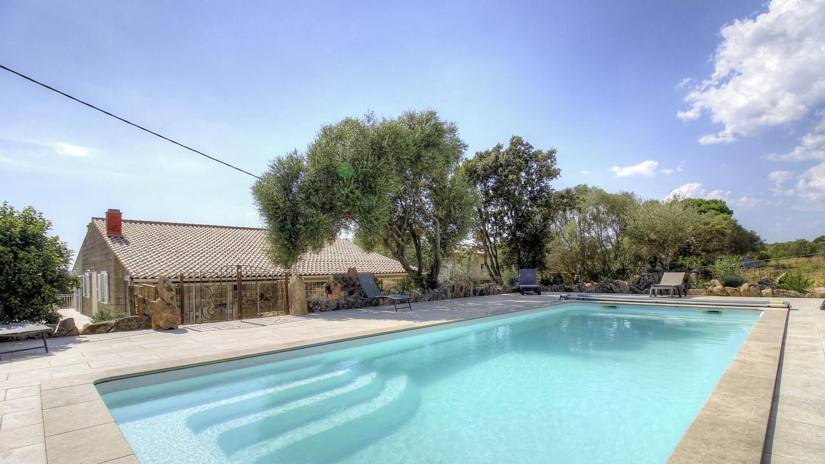 A swimming pool with a stone house and lounge chairs in the background.