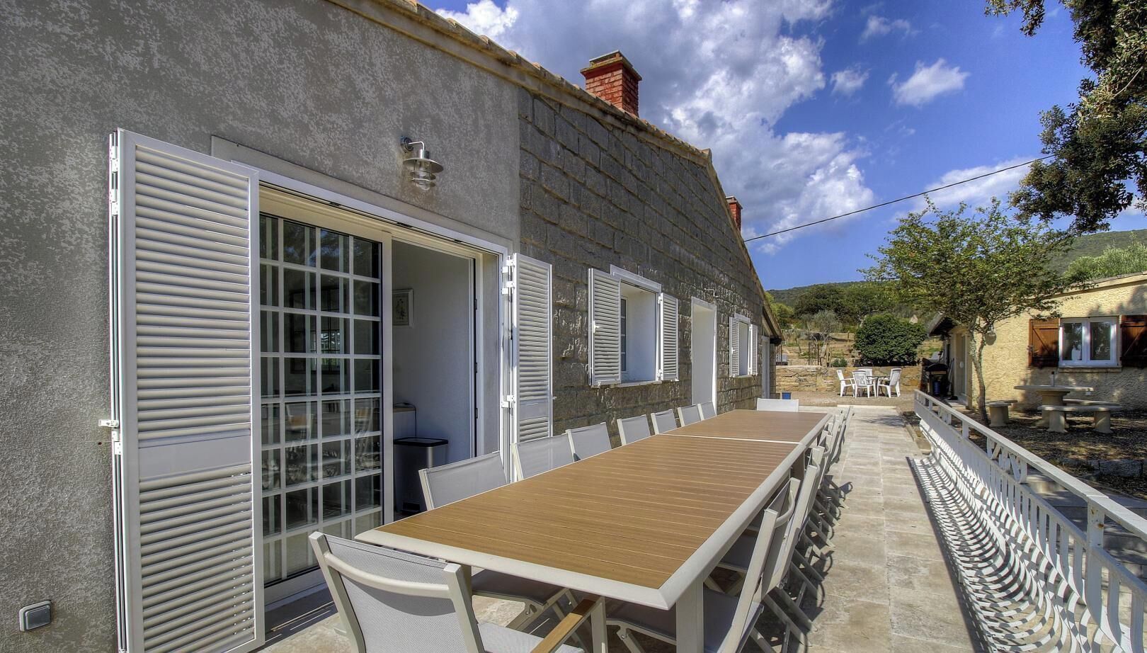 A stone building with a wooden table and chairs outside, a white fence, and a clear sky.