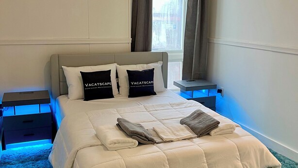 Una cama bien hecha con almohadas, una mesita de noche y una ventana con cortinas.