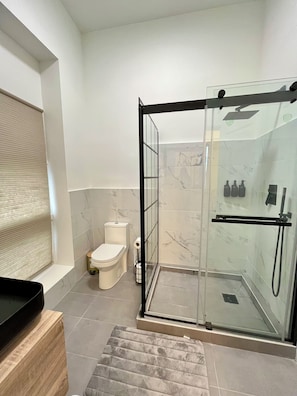 A modern bathroom with a glass-enclosed shower, a toilet, and a sink area.
