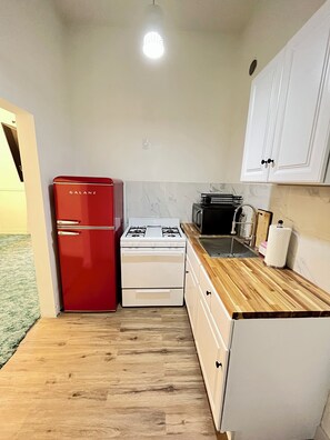 A compact kitchen with a red refrigerator, white stove, and wooden countertop.
