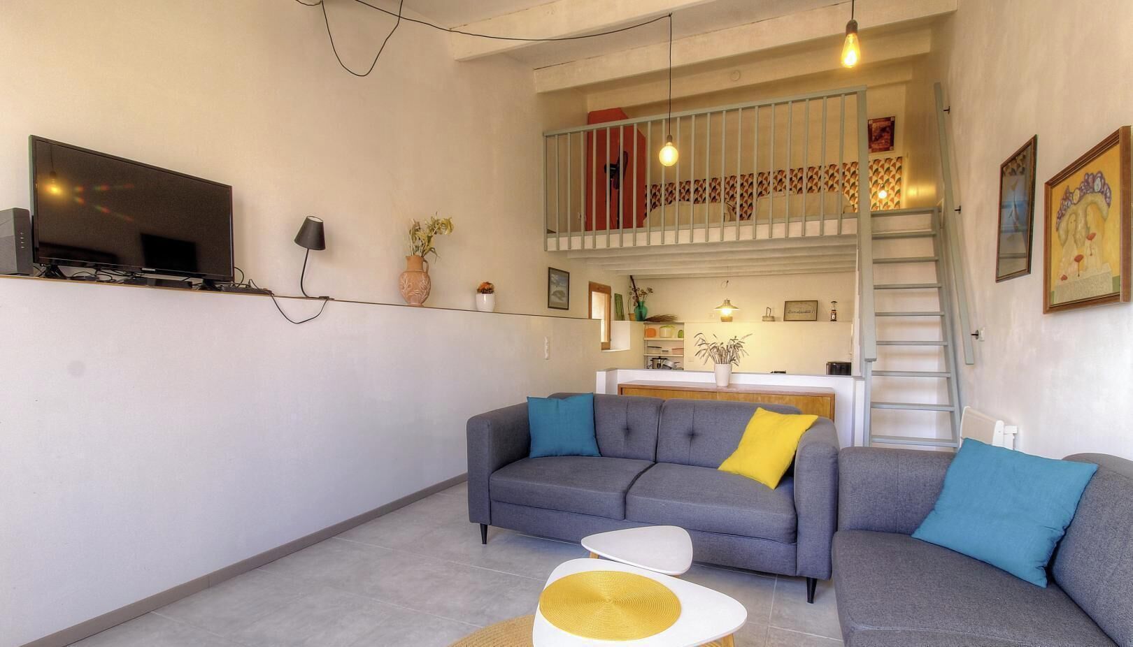 Ein Wohnzimmer mit einem grauen Sofa, einem kleinen weißen Tisch und einem Fernseher an der Wand.