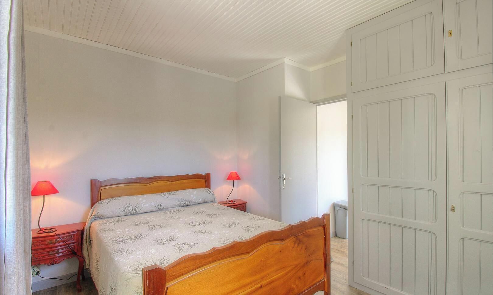 A bedroom with a wooden bed, two bedside lamps, a wardrobe, and a door leading to another room.