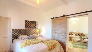 Una camera da letto con un letto, un comodino, una mensola a parete e una porta scorrevole che dà su un soggiorno.