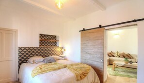 Ein Schlafzimmer mit einem Bett, einem Nachttisch, einem Wandregal und einer Schiebetür zu einem Wohnbereich.
