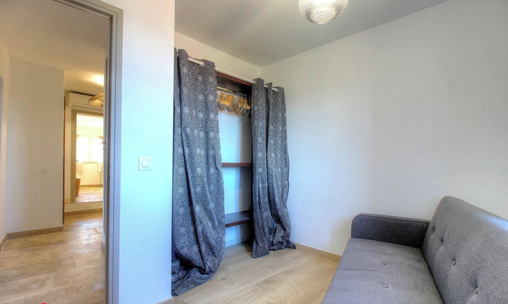 Una habitación con un sofá gris, cortinas estampadas, suelo de madera y una puerta que da a otra estancia.