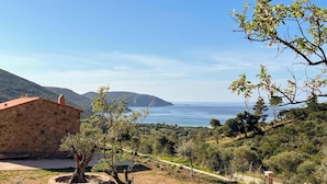 A stone building with a red roof, a tree, and a view of the sea and hills.