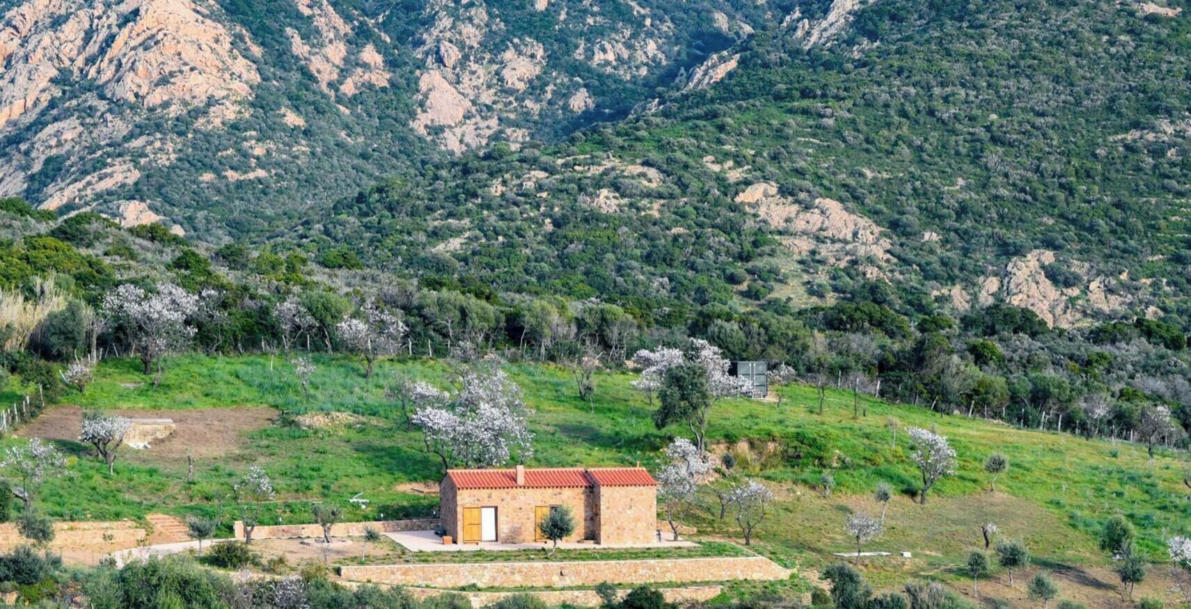 Un edificio de piedra con techo rojo, rodeado de campos verdes y montañas.