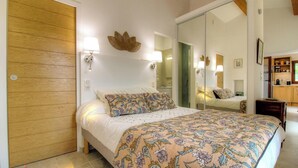 A bedroom with a bed, a wooden door, a mirror, and a wall-mounted lamp.