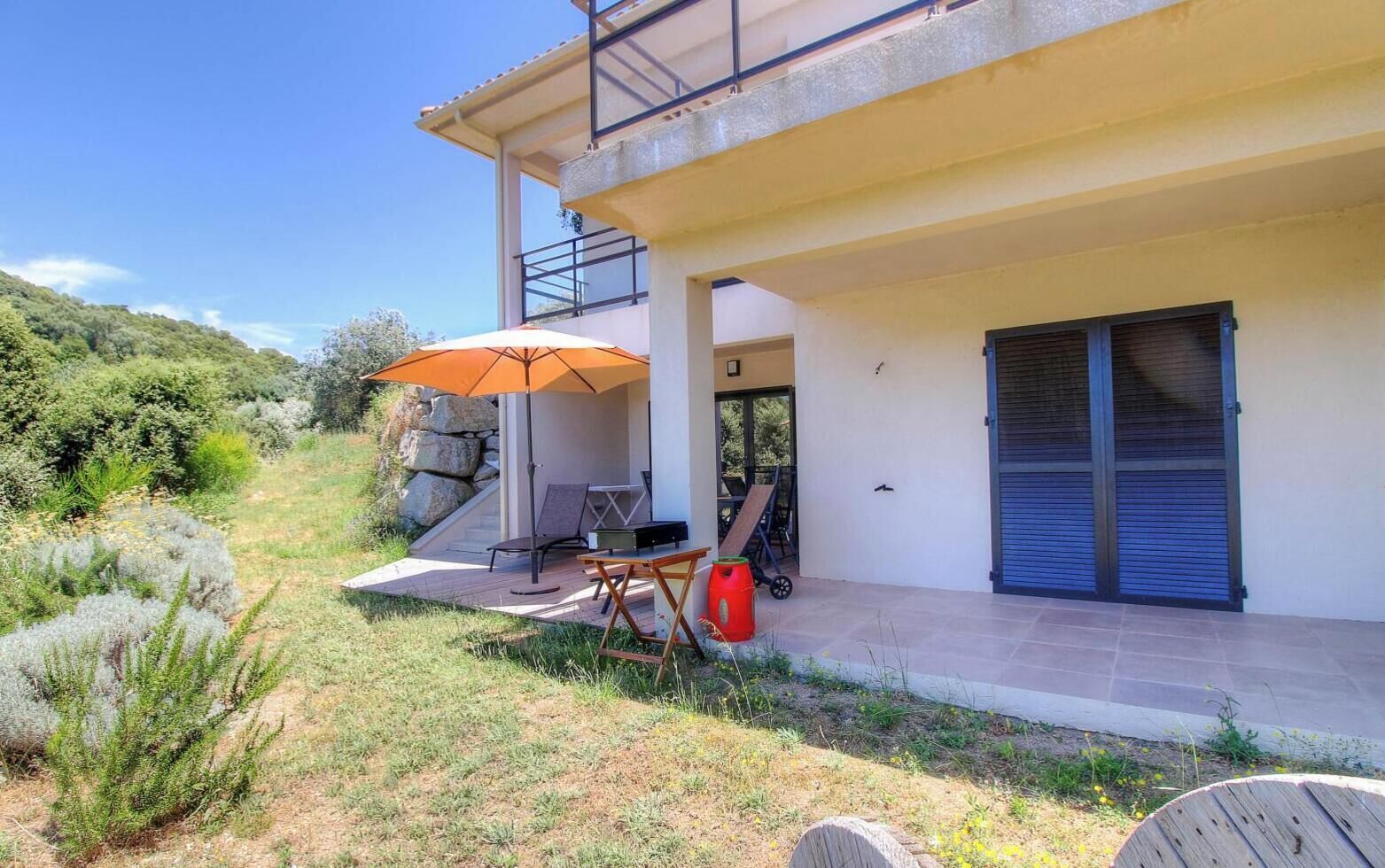 Ein modernes Haus mit Terrasse, Gartenmöbeln und einem großen Sonnenschirm.
