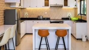 A modern kitchen with white cabinets, a central island with stools, and pendant lighting. - Kigali Savannah Homes and E6 Apartment  (Kigali)