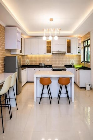 A modern kitchen with white cabinets, a central island with stools, and pendant lighting.