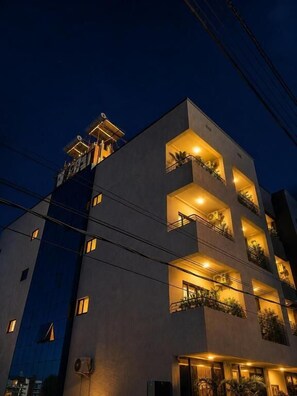 A multi-story building with balconies, a flat roof, and a dark sky.