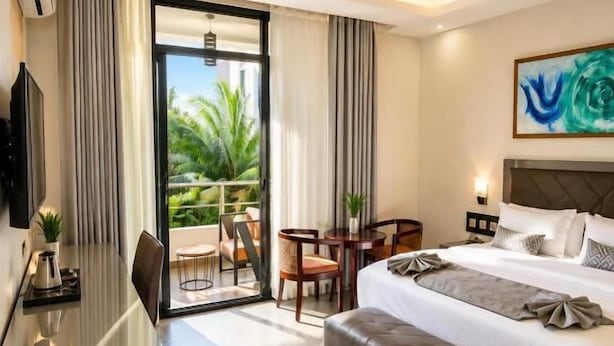 A modern hotel room with a bed, a desk, a chair, a bench, and a balcony with a view. - Kigali Savannah Homes and E6 Apartment  (Kigali)