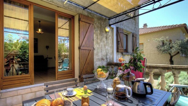 Un balcón con una mesa preparada para el desayuno, una puerta corrediza y vistas al jardín.