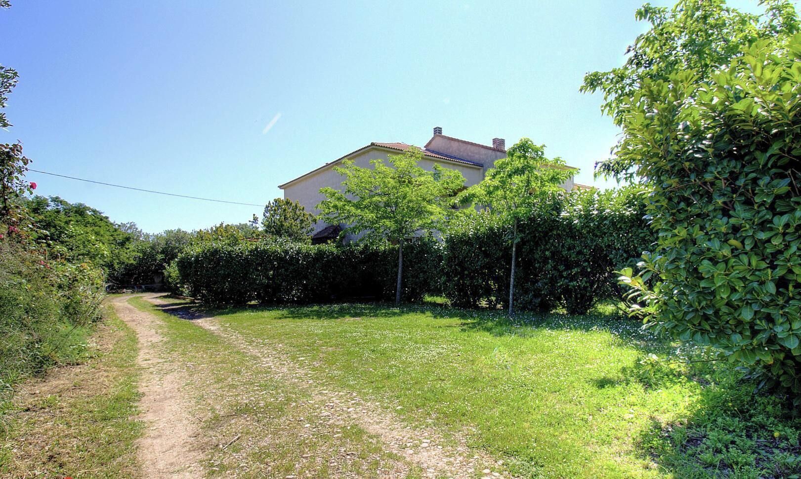 Una proprietà rurale con un sentiero sterrato che conduce a una casa circondata da vegetazione lussureggiante.