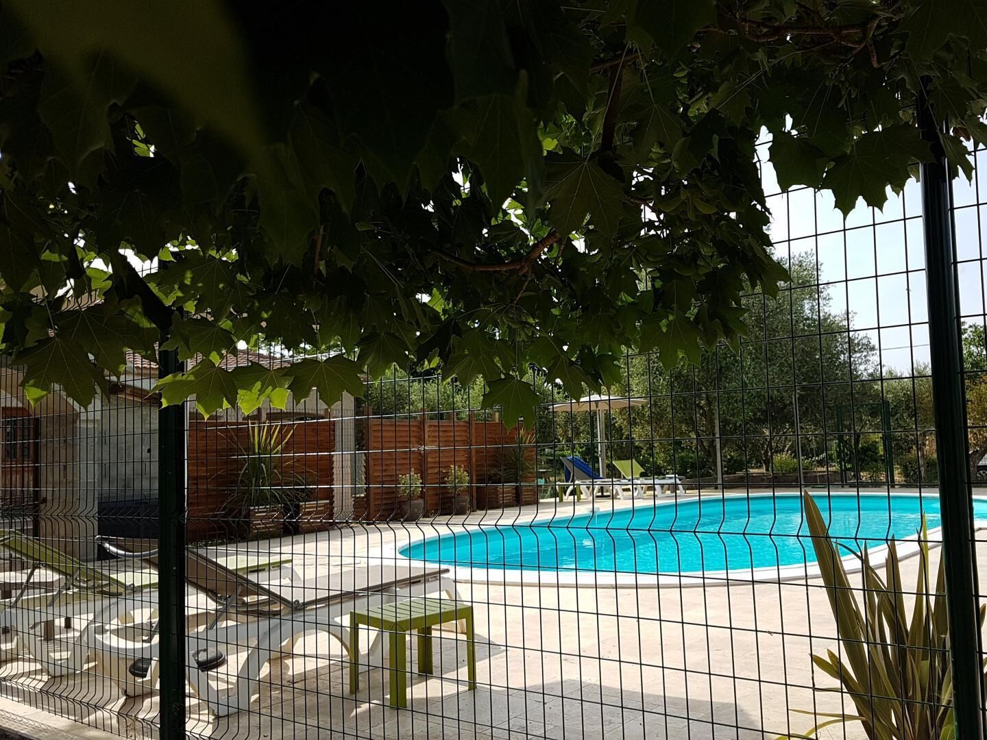 A swimming pool with a fence, lounge chairs, and a covered area.