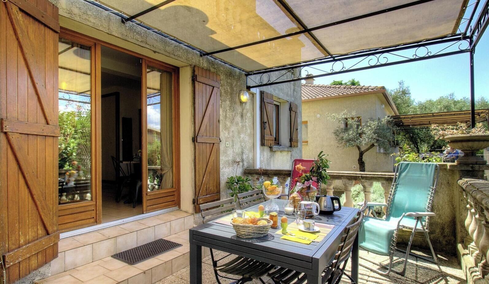 An outdoor patio with a table set for breakfast, a chair, and a view of the garden.