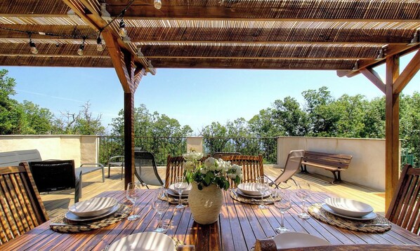 Ein Essbereich im Freien mit einem Holztisch, gedeckt für vier Personen, umgeben von Stühlen, unter einer Holzpergola.