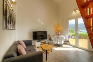 Ein Wohnzimmer mit Sofa, Fernseher, Tisch und einem Balkon mit Aussicht.