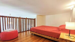 Une chambre avec un lit en bois, un pouf rouge, une table de chevet avec une lampe et une cloison en bois.