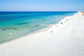 Una platja amb aigua turquesa transparent, sorra blanca i unes quantes cadires i sombrerelles de platja.