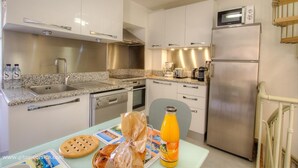 A compact kitchen with a sink, stove, microwave, and refrigerator. There is a table with food items and a bottle of juice. - Bourgada - PIANA - Gîte (PIANA)