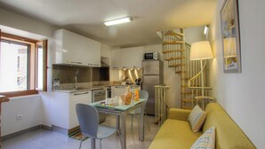 A compact kitchen with a dining area, a sofa, and a staircase. - Bourgada - PIANA - Gîte (PIANA)
