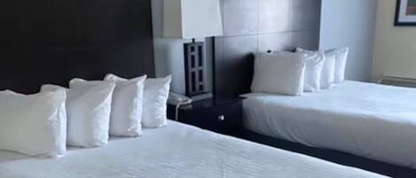 A hotel room with two beds, a dark headboard, a bedside table with a lamp, and a framed picture on the wall.