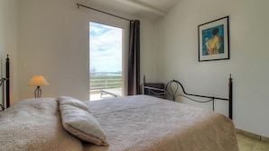 Een slaapkamer met een bed, een lamp, een schilderij en een balkon met uitzicht.