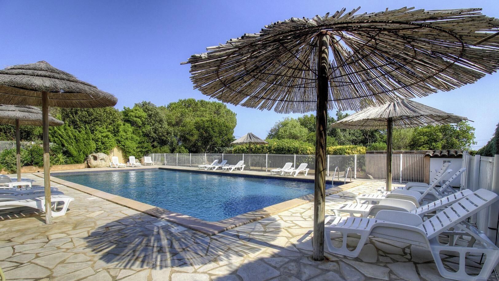 Una piscina con sillas de descanso y sombrillas de paja.