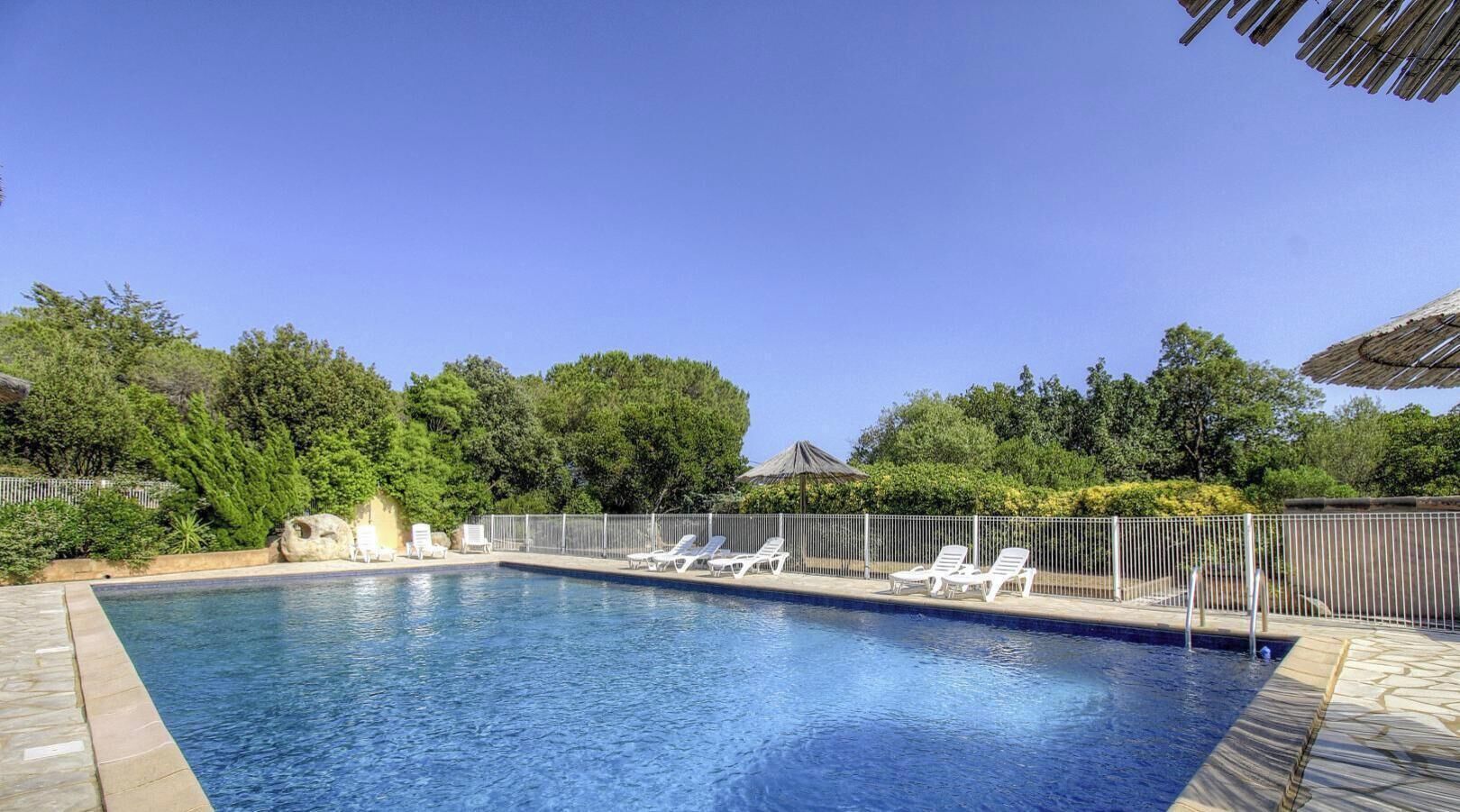 Piscina con sillas de descanso, rodeada por una cerca y árboles.