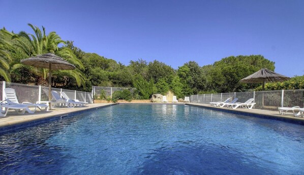 Ein Swimmingpool mit Liegestühlen und Sonnenschirmen, umgeben von viel Grün.