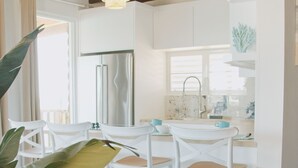 Eine moderne Küche mit weißen Schränken, einem Edelstahlkühlschrank und einem Essbereich mit weißen Stühlen.
