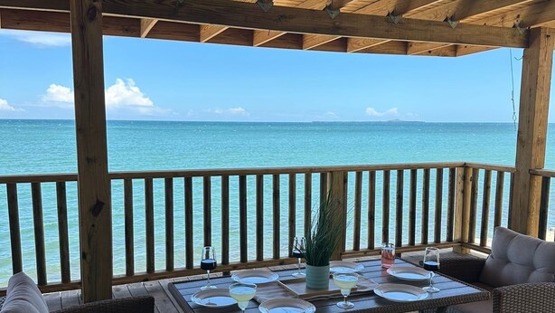 Ein überdachter Außenbereich mit Meerblick, ausgestattet mit Korbmöbeln und einem für das Essen gedeckten Tisch.