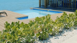Eine Holzterrasse mit Pool, überdachtem Bereich und Blick auf das Meer.