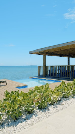 Eine Holzterrasse mit Pool, überdachtem Bereich und Blick auf das Meer.