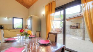A dining area with a table set for four, a vase with flowers, and a view of the outdoor patio. - San Petru - SOCCIA - Gîte (SOCCIA)