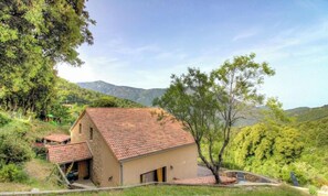 A rustic stone building with a tiled roof, surrounded by lush greenery and hills in the background. - San Petru - SOCCIA - Gîte (SOCCIA)